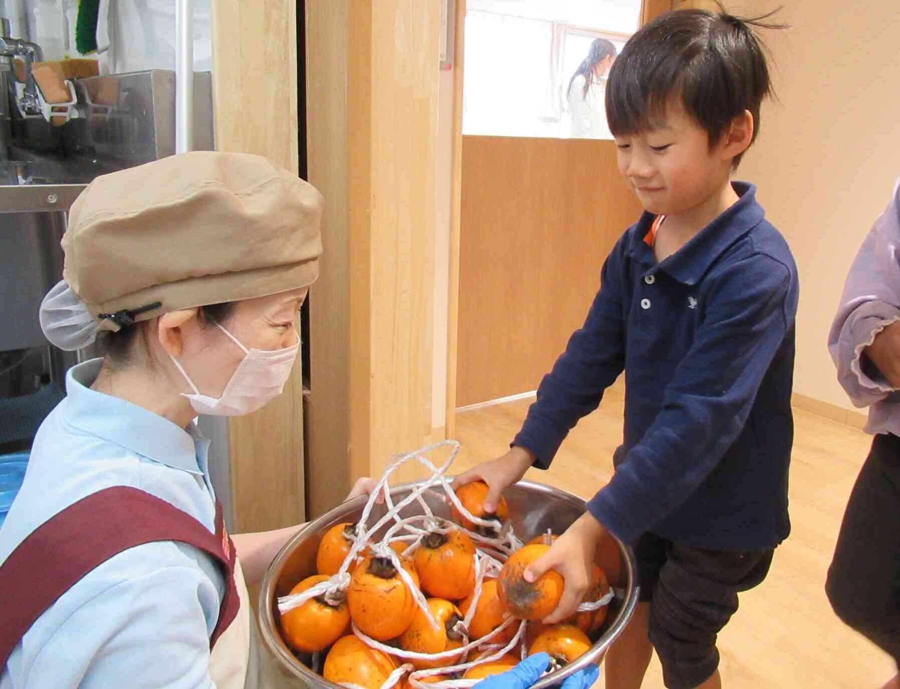 給食の先生に柿の皮をむいてもらいます。「お願いします！」「甘い柿になりますように・・・♡」そんな願いもこめて給食の先生に柿を託しました。