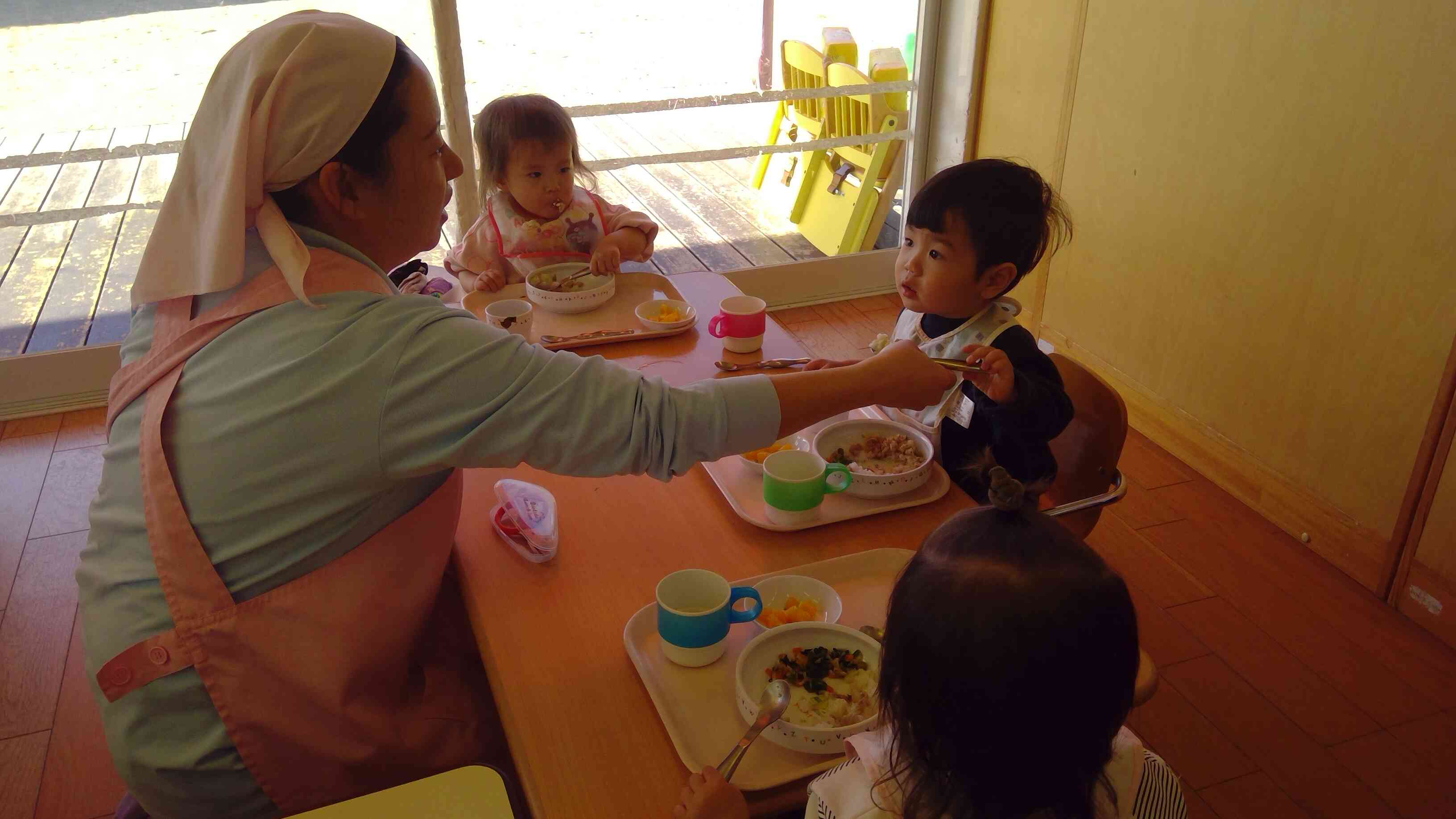 保育者に手伝ってもらいながら、「自分で！」と食べるひよこぐみさん（0歳児）