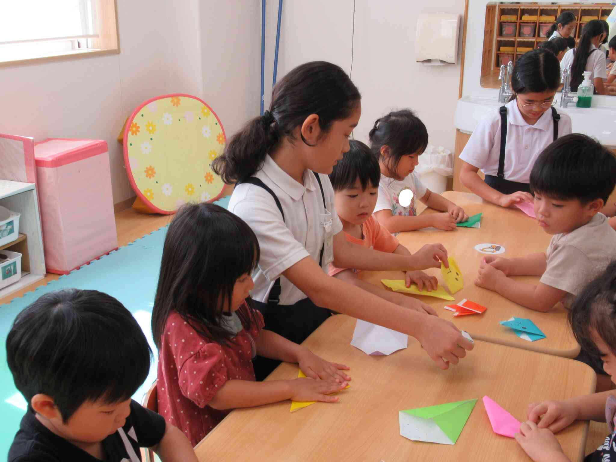 折り紙の折り方を教えるのは大人でも難しいですが、、、子どもたちよく聞いています。お姉ちゃん先生頑張って！