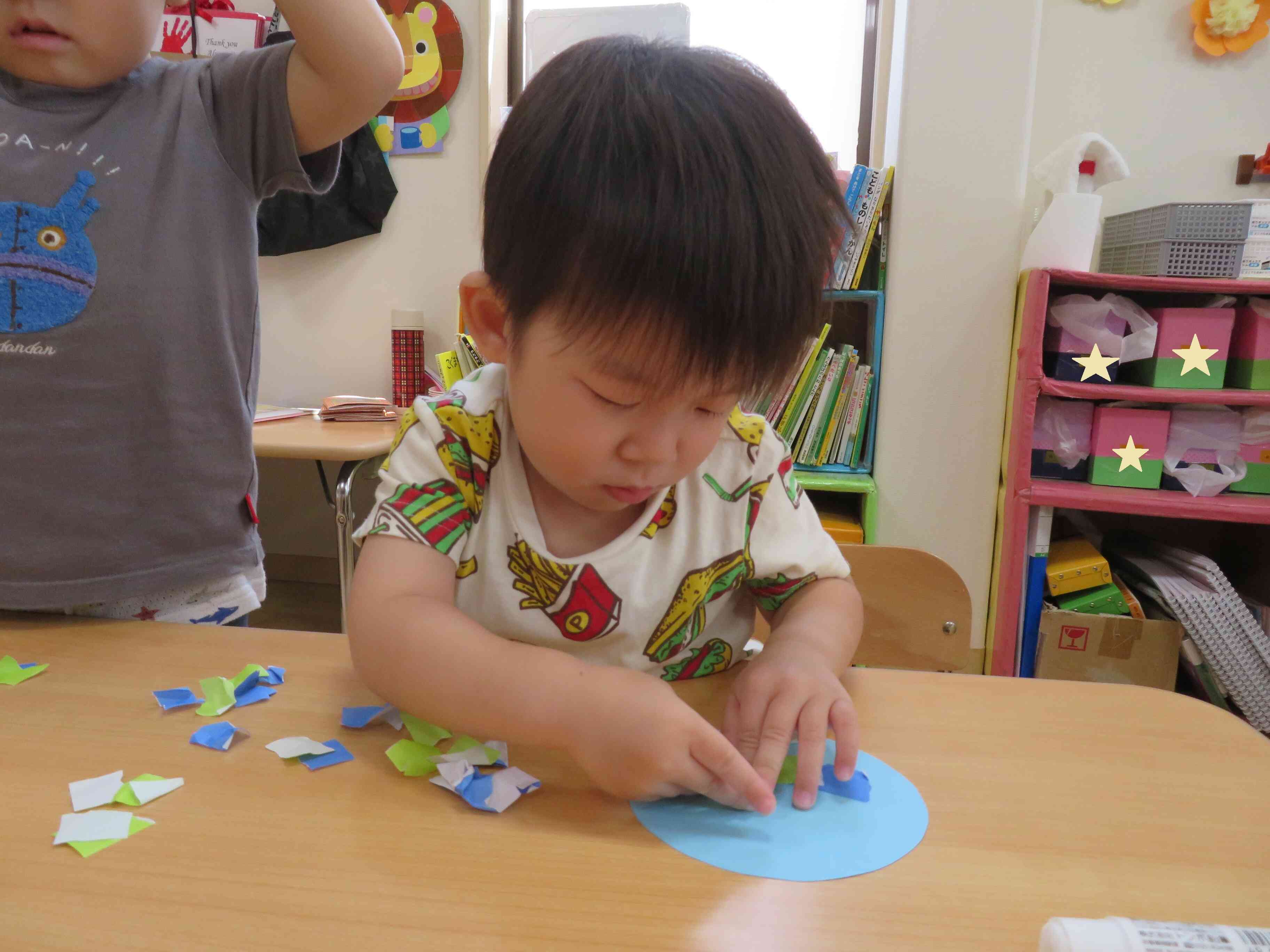 2歳児さんの造形遊びはじっくり楽しみます。最初に折り紙を自分でびりびりちぎって、次はのりで貼っていくよ。