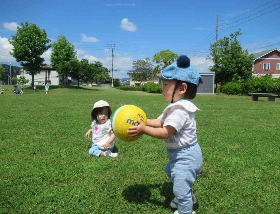 緑いっぱいの公園でボール転がしを楽しんでいる0歳児です。天候もよくすがすがしい風も吹き気持ちいいね！